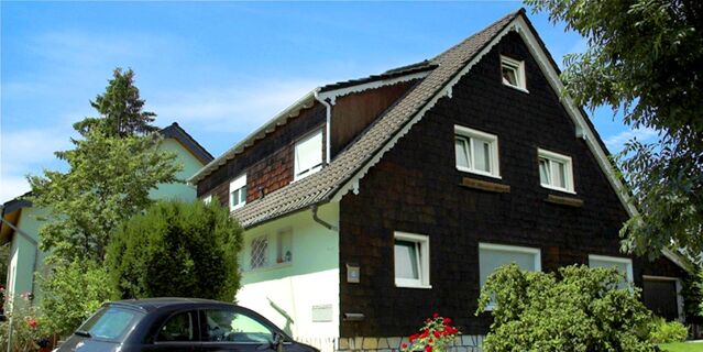 Au&szlig;enansicht des G&auml;stehaus Boardinghouse Stapf mit dunklem Holzgiebel und begr&uuml;nter Umgebung an sonnigem Tag.