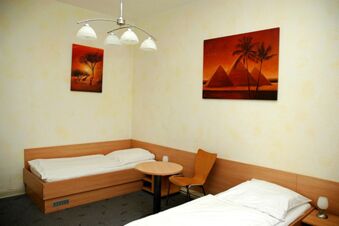 Ein schlicht eingerichtetes Zimmer mit zwei Einzelbetten, rundem Tisch und Wandbildern im G&auml;stehaus Boardinghouse Stapf.