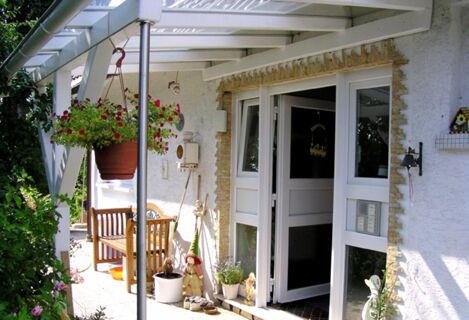 Eingangsbereich mit &uuml;berdachter Terrasse und sch&ouml;ner Bepflanzung beim G&auml;stehaus Boardinghouse Stapf, einladend und gem&uuml;tlich gestaltet.