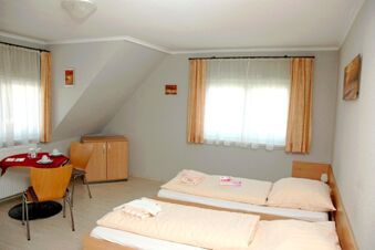 Helles und schlicht eingerichtetes Doppelzimmer im G&auml;stehaus Boardinghouse Stapf mit zwei Betten und einem kleinen Tisch mit St&uuml;hlen.