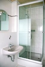 Kompaktes Badezimmer mit Waschbecken und Duschkabine im G&auml;stehaus Boardinghouse Stapf, gepflegte und helle Fliesenw&auml;nde.
