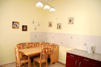 Kleine K&uuml;che mit Eckbank, Tisch, St&uuml;hlen, Wanddekoration und Wasserkocher im G&auml;stehaus Boardinghouse Stapf in warmen Farben.
