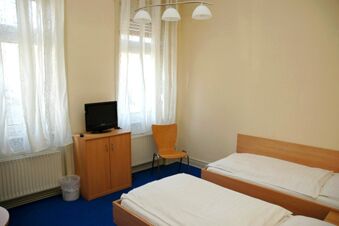 Helles Zimmer mit zwei Betten, einem Stuhl, Fernseher auf Kommode und wei&szlig;en Gardinen im G&auml;stehaus Boardinghouse Stapf.