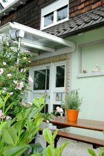 Eingangsbereich mit Sitzbank, Pflanzen und Blumendekoration am G&auml;stehaus Boardinghouse Stapf mit sichtbarer T&uuml;r und Fenster.