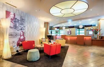 Heller und einladender Empfangsbereich mit farbigen Sesseln, moderner Beleuchtung und Kunstwerken im Leonardo Hotel Mannheim City Centre.