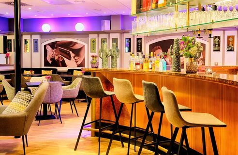 Barbereich mit Theke, Barhockern und Sitzpl&auml;tzen im stilvollen Ambiente des Leonardo Hotel Mannheim City Centre mit moderner Beleuchtung und Dekoration.