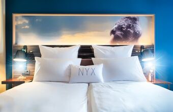 Modernes Doppelzimmer im NYX Hotel Mannheim mit zwei Betten, wei&szlig;en Kissen und dekorativem Adlerbild &uuml;ber dem Kopfteil.