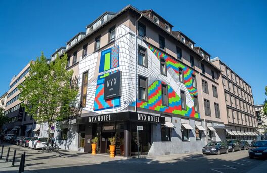 Die farbenfrohe Fassade des NYX Hotel Mannheim mit geometrischem Kunstwerk an einem sonnigen Tag in der Innenstadt.