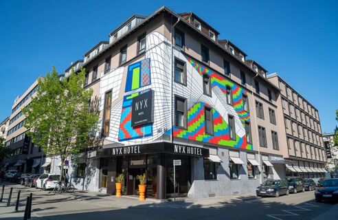 Die farbenfrohe Fassade des NYX Hotel Mannheim mit geometrischem Kunstwerk an einem sonnigen Tag in der Innenstadt.