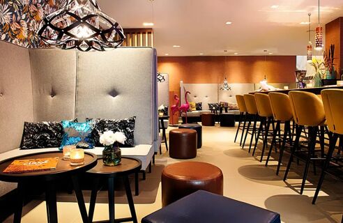 Moderne Lounge mit bequemen Sitzb&auml;nken, Barhockern und dekorativem Licht im NYX Hotel Mannheim f&uuml;r entspannte Momente.