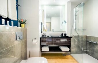 Modernes und helles Badezimmer mit Dusche, Waschtisch und Toilette im NYX Hotel Mannheim, stilvoll und sauber eingerichtet.