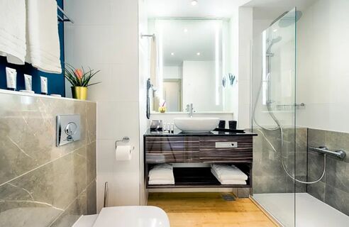 Modernes und helles Badezimmer mit Dusche, Waschtisch und Toilette im NYX Hotel Mannheim, stilvoll und sauber eingerichtet.