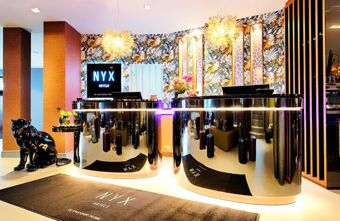 Moderne Rezeption mit gl&auml;nzenden schwarzen Theken, einem bunt gemusterten Hintergrund und Skulptur im Eingangsbereich des NYX Hotel Mannheim.