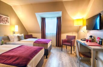 Gem&uuml;tliches Zimmer im Leonardo Hotel Mannheim-Ladenburg mit zwei Einzelbetten, Schreibtisch, Fernseher und gem&uuml;tlicher Beleuchtung.