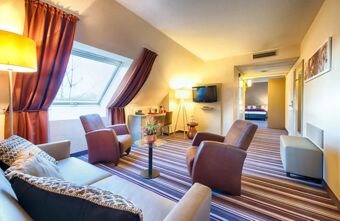 Helles Wohnzimmer mit gem&uuml;tlichen Sesseln, Sofa und Fenster im Dachgeschoss des Leonardo Hotel Mannheim-Ladenburg mit modernem Ambiente.