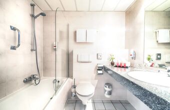 Helles Badezimmer mit Dusche, Badewanne, Toilette und Waschtisch im Leonardo Hotel Mannheim-Ladenburg mit modernen Armaturen und guter Ausstattung.
