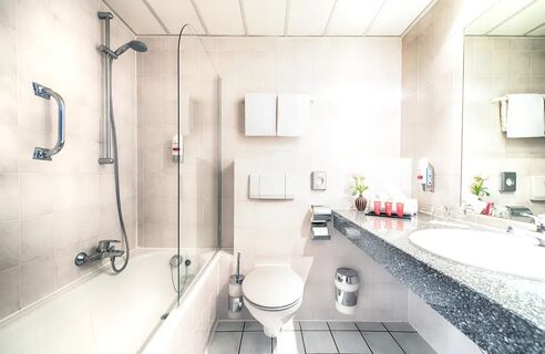 Helles Badezimmer mit Dusche, Badewanne, Toilette und Waschtisch im Leonardo Hotel Mannheim-Ladenburg mit modernen Armaturen und guter Ausstattung.