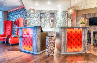 Stylische Lobby des Leonardo Hotel Mannheim-Ladenburg mit roten Sitzgelegenheiten, modernen Empfangstheken und floralem Dekor an den W&auml;nden.