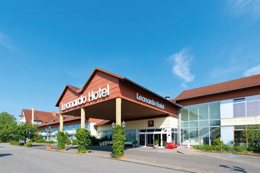 Leonardo Hotel Heidelberg-Walldorf entrance with a covered driveway, red roof, glass windows, and clear blue sky background