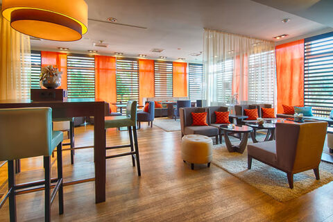 Spacious lounge area at Leonardo Hotel Heidelberg-Walldorf with orange curtains, modern seating, tables, and large pendant light fixtures