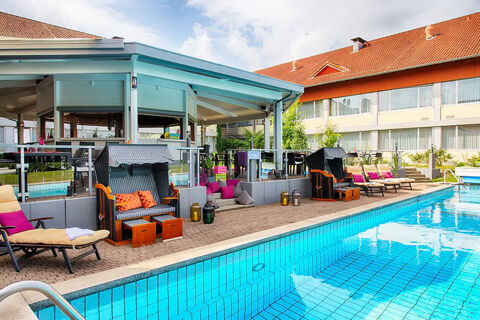 Outdoor swimming pool with sun loungers, wicker beach chairs, and a covered seating area at Leonardo Hotel Heidelberg-Walldorf