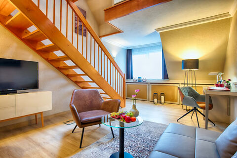 Modern living area with wooden staircase, brown armchair, glass coffee table, TV, and workspace in Leonardo Hotel Heidelberg-Walldorf