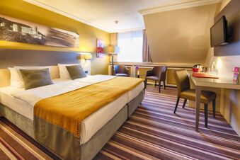 Hotel room at Leonardo Hotel Heidelberg-Walldorf with a double bed, striped carpet, two chairs, desk, and mounted TV
