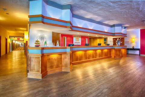 Reception desk area with wood paneling, blue and orange accents, glasses, and a fruit stand at Leonardo Hotel Heidelberg-Walldorf