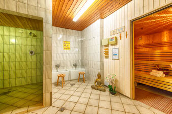 A tiled sauna area at Leonardo Hotel Heidelberg-Walldorf with a wooden sauna interior, two stools by wash basins, and a Buddha statue