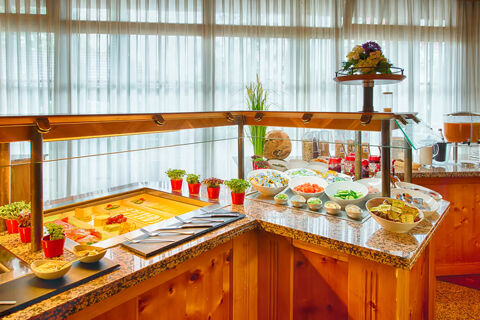 Buffet setup with sliced vegetables, cheeses, spreads, cereals, and herbs on a granite counter at Leonardo Hotel Heidelberg-Walldorf