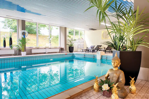 Indoor swimming pool at Leonardo Hotel Heidelberg-Walldorf with blue tiled pool, lounge chairs, plants, and Buddha statue decor