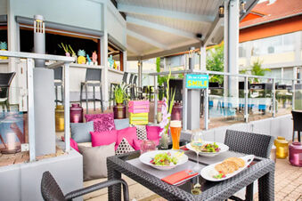 Outdoor patio dining area at Leonardo Hotel Heidelberg-Walldorf with black wicker chairs, salads, bread, and drinks on the table