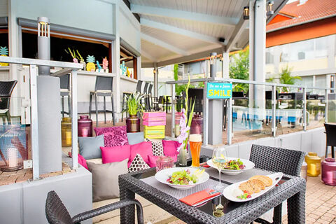 Outdoor patio dining area at Leonardo Hotel Heidelberg-Walldorf with black wicker chairs, salads, bread, and drinks on the table