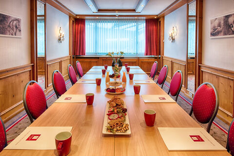 Meeting room at Leonardo Hotel Heidelberg-Walldorf with wooden table, red chairs, snacks, cups, and notepads arranged neatly