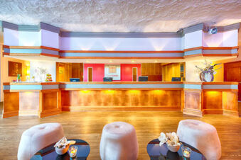 Reception area of Leonardo Hotel Heidelberg-Walldorf with wood paneling, three computer monitors, and three beige stools by round tables