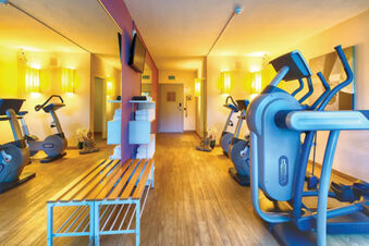 Fitness room at Leonardo Hotel Heidelberg-Walldorf with exercise bikes, elliptical machine, bench, and towels on shelves