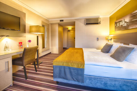 Hotel room at Leonardo Hotel Heidelberg-Walldorf with a double bed, striped carpet, desk, chair, and wall-mounted TV