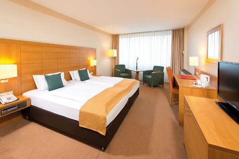 Hotel room at Leonardo Hotel Heidelberg-Walldorf with twin beds, green armchairs, wooden desk, TV and window with white curtains