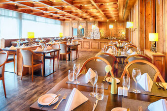 Dining area of Leonardo Hotel Heidelberg-Walldorf with wooden furniture, folded napkins, glasses, and warm lighting fixtures