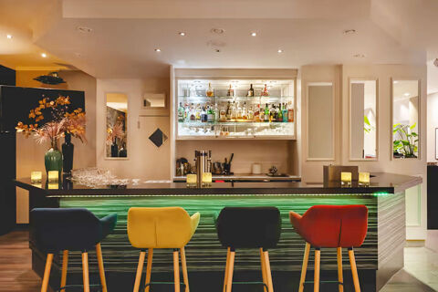 Interior view of a modern bar with a backlit counter and colorful chairs in Leonardo Hotel Heidelberg City Center