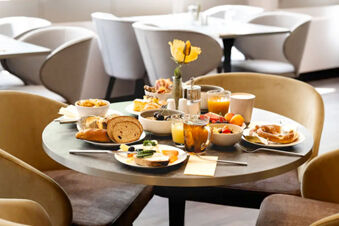Round table with assorted breakfast foods and drinks including bread, pastries, juice, and tea at Leonardo Hotel Heidelberg City Center