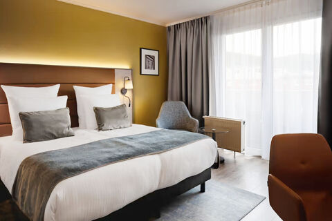 Hotel bedroom at Leonardo Hotel Heidelberg City Center with double bed, gray and white bedding, armchairs, and sheer curtains