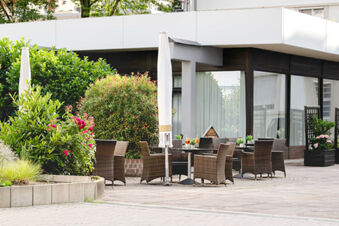 Outdoor patio area with wicker chairs, tables, umbrellas, and greenery at Leonardo Hotel Heidelberg City Center