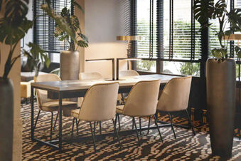 Dining area with six beige chairs around a rectangular table and two tall vases with plants at Leonardo Hotel Heidelberg City Center