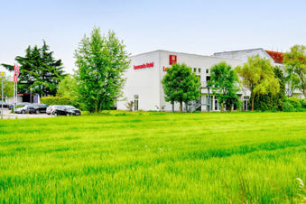 Green grassy field in front of a white building with red Leonardo Hotel Heidelberg signage and surrounding leafy trees