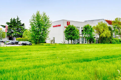Green grassy field in front of a white building with red Leonardo Hotel Heidelberg signage and surrounding leafy trees