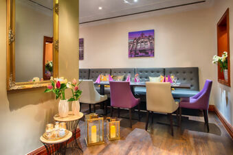Dining area at Leonardo Hotel Heidelberg with purple and beige chairs, tufted bench, and floral decorations on wooden floor