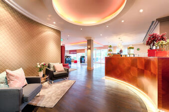 Leonardo Hotel Heidelberg reception area with curved wooden desk, gray sofas with cushions, floral decorations, and warm lighting