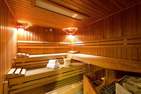 Interior view of a wooden sauna room with benches, towels, a bucket, and a ladle at Leonardo Hotel Heidelberg
