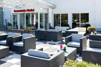 Outdoor seating area with black wicker chairs and white cushions in front of Leonardo Hotel Heidelberg entrance